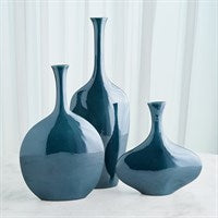 Three glossy Silhouette Reactive Vases Blue by Global Views/Surya, crafted in Portuguese ceramic with a rich blue glaze, stand at varying heights on a light surface, complemented by a soft white curtain in the background.