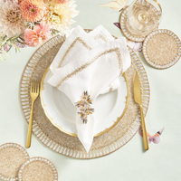 Elegant table setting with gold utensils, a white plate with gold trim, embroidered napkins accented by Kim Seybert’s Butterflies Napkin Ring Set of 4, gold and beaded placemats and coasters, a glass of wine, and pink and cream flowers.