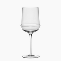 The Dune White Wine Glass by Serax features a clear, modern design with an angular bowl and a distinctive horizontal ridge encircling the middle. This artisanal glass is finished with a long, slender stem and rests on a flat base, shown here against a white background.