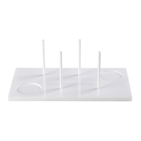 The Acrylic Bagels On Board Tray - White by Inspired Generations is a white rectangular acrylic tray featuring four vertical rods and two circular indents, perfect for organizing or holding items upright—an ideal and stylish choice for serving bagels at your next brunch board.