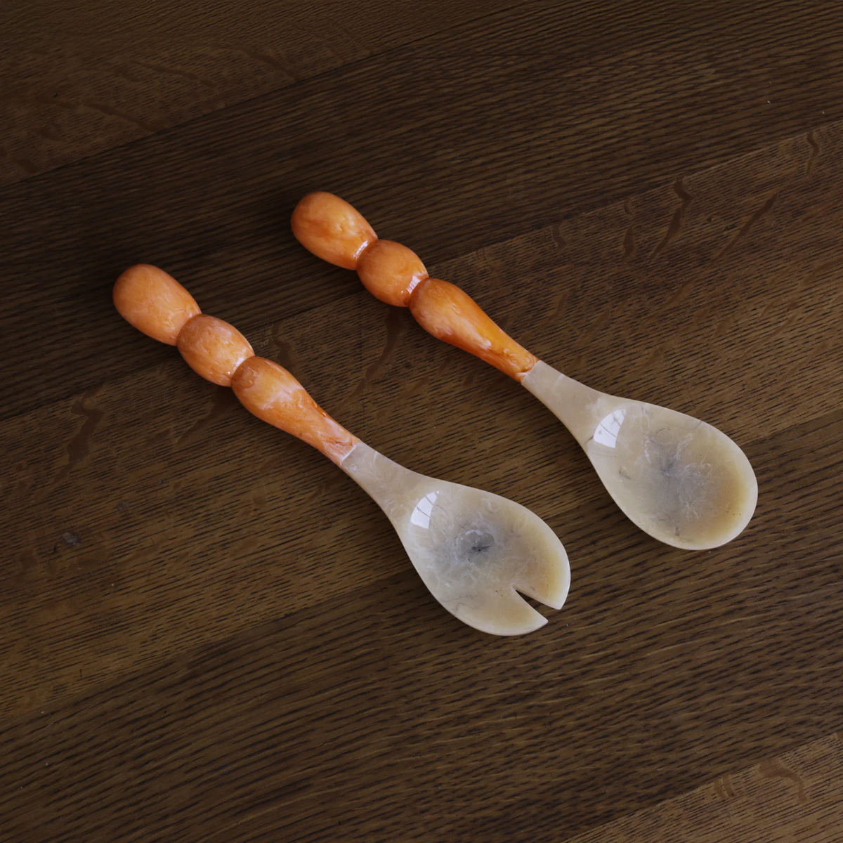 The Beatriz Ball Resin Rio Bubble Salad Servers feature rounded bubble handles and translucent, horn-like scoops—one slotted, one solid—resting on a dark wooden surface.
