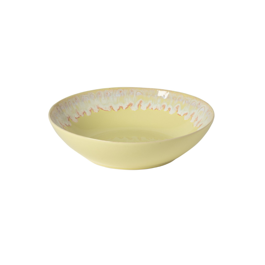 The Costa Nova Taormina Dinnerware Yellow bowl, with its shallow, round shape and wavy orange and blue rim design, showcases contemporary ceramic tableware against a plain white background.