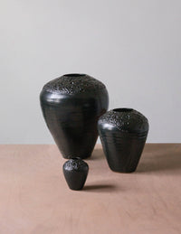 The Esme Crawl Vase - Black Lava by Kalya OD Studio features textured tops in large and medium sizes. Stylish and water safe, these black ceramic vases are arranged on a light wooden surface against a plain background.