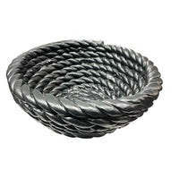The Tissit Bowl Matte Black by Schwung Design is a round ceramic piece with a thick twisted rope spiral design, matte black finish, and smooth texture—serving as a striking modern accent against a white backdrop.