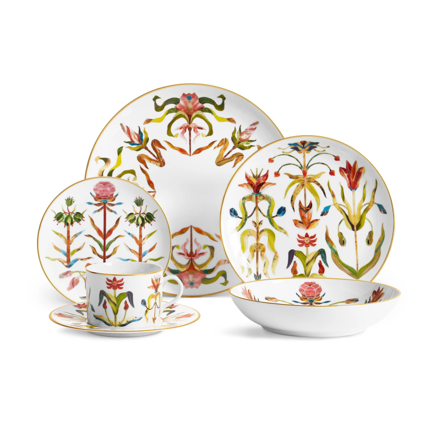 L’Objet Grand Tour Dinnerware set featuring handcrafted porcelain with 24k gold rims and colorful, symmetrical floral patterns, including a dinner plate, salad plate, teacup and saucer, and a shallow bowl.