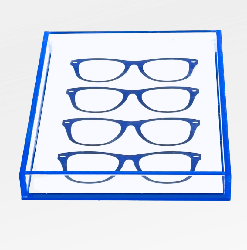 The Eye Candy Specs Eyeglass Tray is a transparent acrylic holder with a blue border, designed to display four pairs of blue eyeglass frames in parallel rows on a white background.