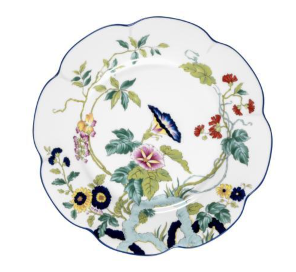 The Nymphea Paradis Bleu plate by Royal Limoges features a white scalloped design with vibrant flowers, green leaves, delicate branches, and is finished with a blue rim highlighting its porcelain artistry.