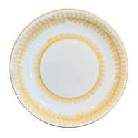 The Marie Daâge Rafia 5 Dinnerware by Marie Daâge features a round white porcelain plate with a hand-painted yellow and gold radial pattern on the rim and inner circle, elegantly crafted in France and shown from above on a white background.