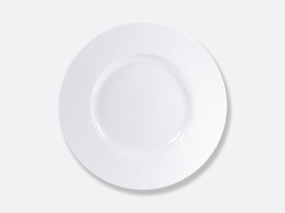 The Ecume White Dinnerware by Bernardaud is a round, white plate with a wide, textured rim, crafted in France from fine Limoges porcelain and shown from above on a plain light gray background.