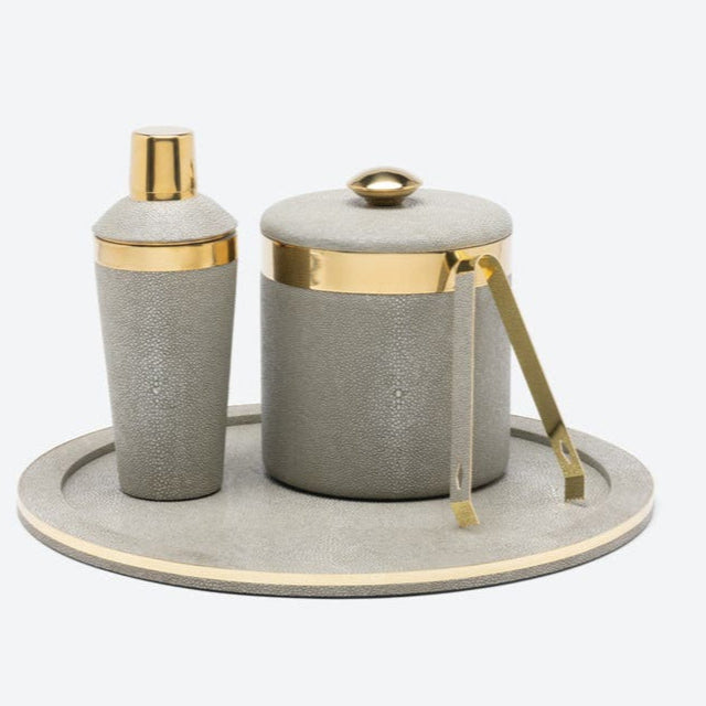 A gray stingray cocktail shaker, ice bucket with tongs, and the Blue Pheasant Langston Round Tray in Sand/Gold—an elegant serving piece with gold accents and a chic faux shagreen finish.