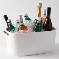 The Tina Frey Large Bucket With Leather Handle, filled with ice, chills sparkling water, white wine, rosé, and champagne—each bottle glistening with condensation on a white surface, ready for any celebration.