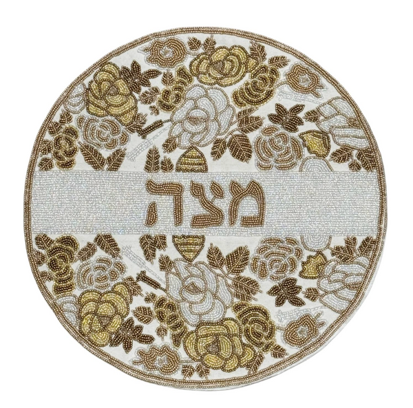 The Lyss & Kat Hebrew Floral Beaded Matzah Cover - Gold is a round matzah cover featuring hand-beaded gold and white floral patterns with the Hebrew word מצה (matzah) in the center, making it an elegant addition to your Passover table decor.