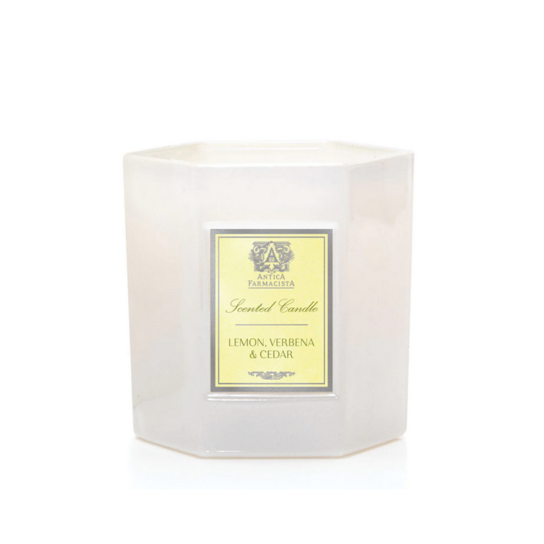 A white, hexagonal candle jar with a yellow label reading "Lemon Verbena & Cedar Candle" by Antica Farmacista/Harper is displayed against a plain white background.