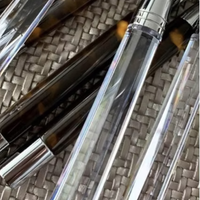 Several empty clear plastic lip gloss tubes with silver caps sit on a woven surface beside the Capdeco Doric Flatware 5 Piece Setting - Clear, creating an elegant and contemporary vibe in natural light.