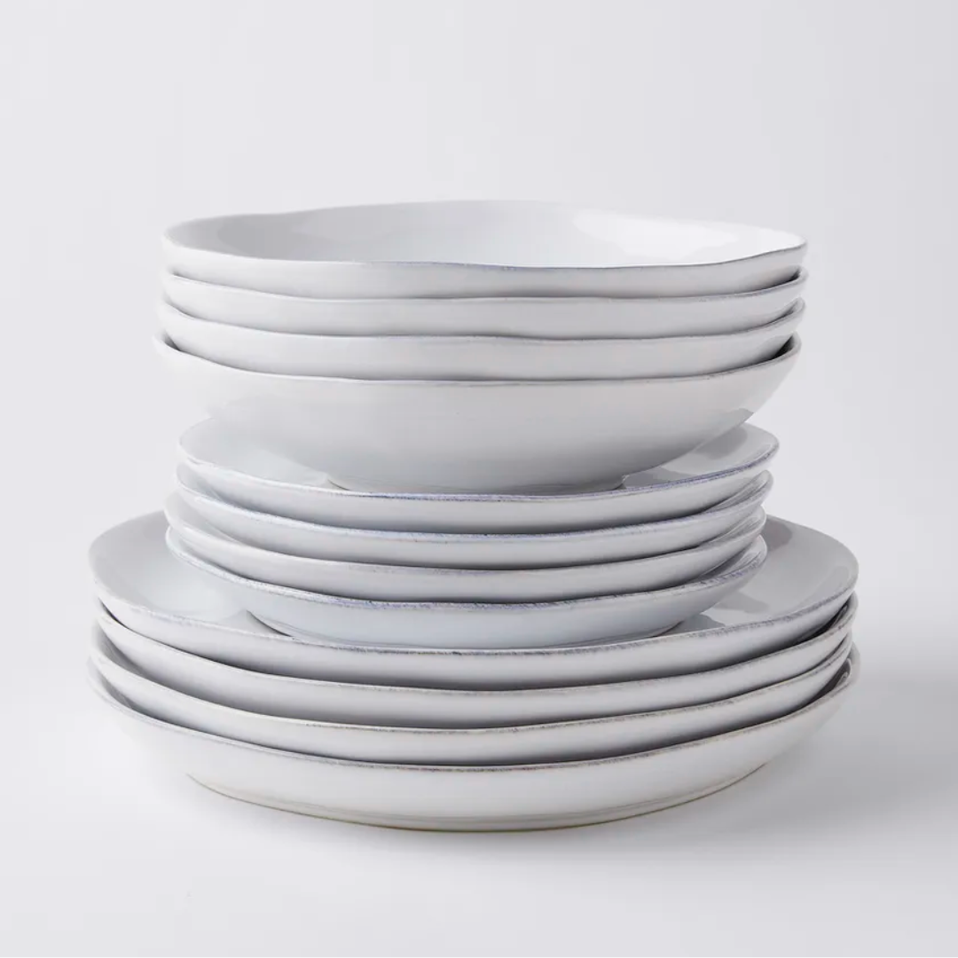 The Livia Dinnerware White by Casafina/Costa Nova features artisan-crafted white stoneware bowls and plates with uneven edges, neatly arranged on a plain white background. This modern tableware is beautifully crafted in Portugal.