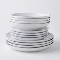 The Livia Dinnerware White by Casafina/Costa Nova features artisan-crafted white stoneware bowls and plates with uneven edges, neatly arranged on a plain white background. This modern tableware is beautifully crafted in Portugal.