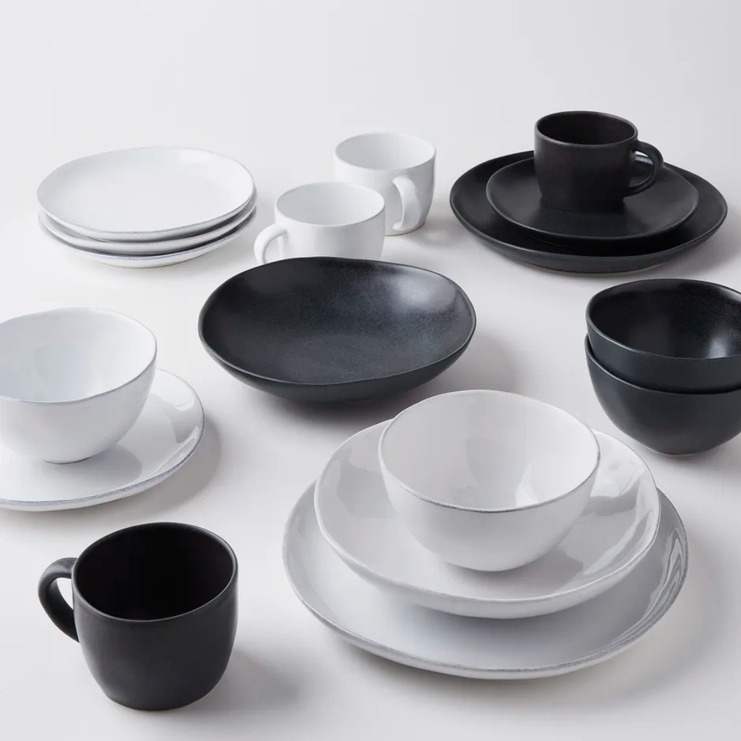 The Livia Dinnerware Matte Black collection by Casafina/Costa Nova features stoneware plates, bowls, and cups in black and white, arranged in matching pairs on a white surface.
