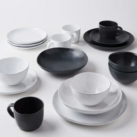 The Livia Dinnerware Matte Black collection by Casafina/Costa Nova features stoneware plates, bowls, and cups in black and white, arranged in matching pairs on a white surface.