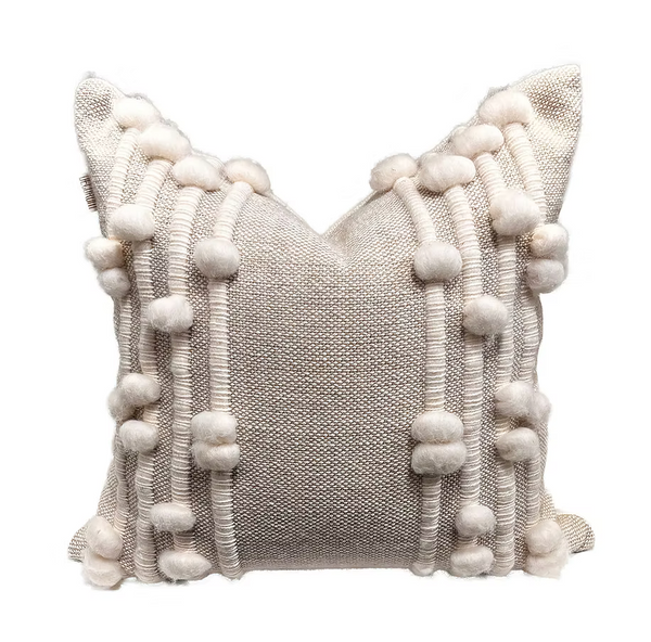 The Decorum Wooly Bumps Pillow - Sand / White is a handcrafted square cushion with textured beige fabric, vertical rows of fluffy white pom-poms, and woven ridges—perfect for adding cozy style to any home.