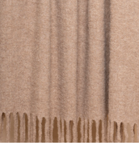 A close-up of the Thread & Butter Brushed Boucle Throw, a beige blanket with a soft, textured finish and long, even fringe, offering a natural sheen and luxurious feel reminiscent of Baby Alpaca blankets.