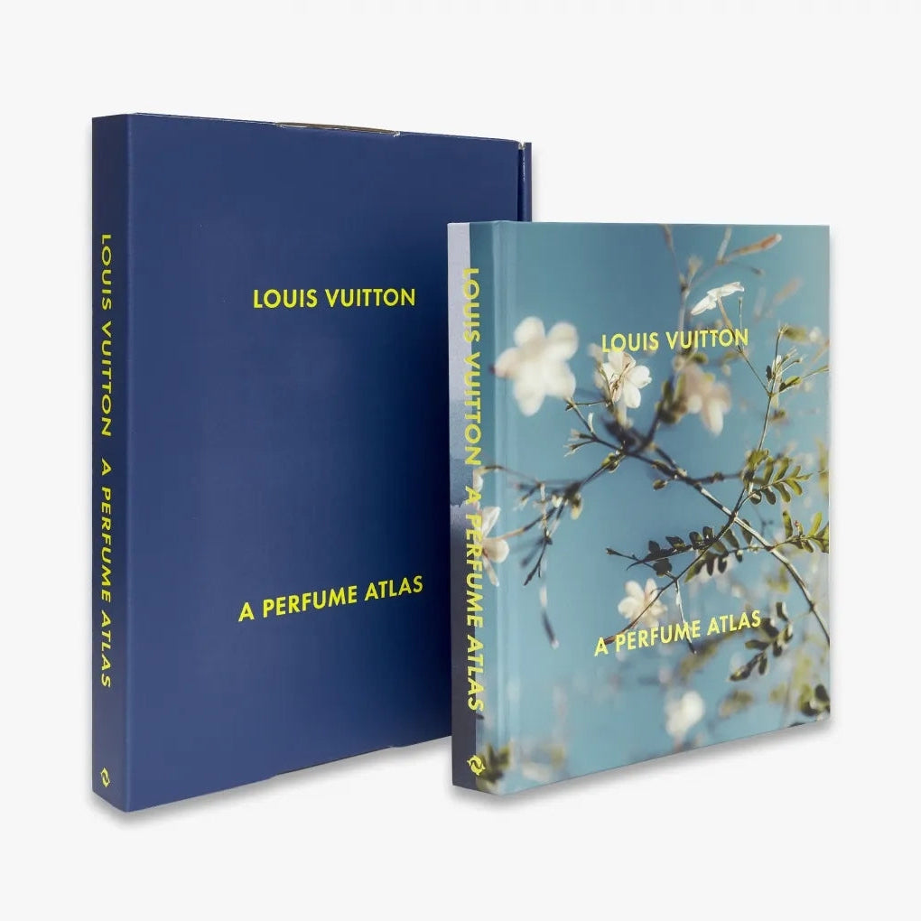 Louis Vuitton: A Perfume Atlas by W.W. Norton Company features a blue slipcase with yellow text, and a cover adorned with white and yellow flowers reflecting fragrance ingredients explored in this perfumery book.