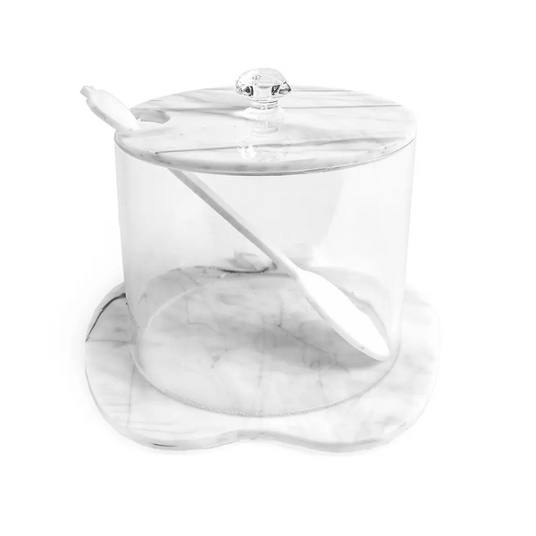 The BT- Shalom Lucite Apple Honey Jar with Spoon is a clear, cylindrical jar featuring stylish marble accents on the lid and base, plus a slot for the included white spoon that fits neatly inside.