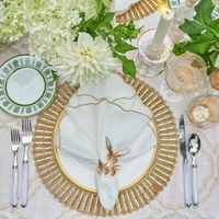 Elegant table setting featuring Kim Seybert's Luminance Napkin in White & Gold, paired with a gold placemat, white and gold plate, floral napkin ring, cutlery, glassware, green-accented china, white flowers, and a lit candle.