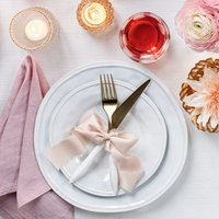 A place setting featuring Vietri's Aria Dinnerware, gold cutlery tied with a pink ribbon, a pink napkin, candles, a drink, and flowers.