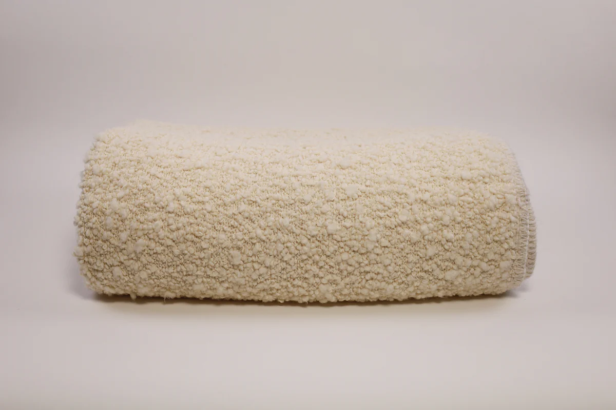 The Uniquity Kusama Boucle Cream Throw, a fluffy luxury throw in cream, is displayed rolled-up on a simple light background.