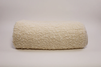 The Uniquity Kusama Boucle Cream Throw, a fluffy luxury throw in cream, is displayed rolled-up on a simple light background.