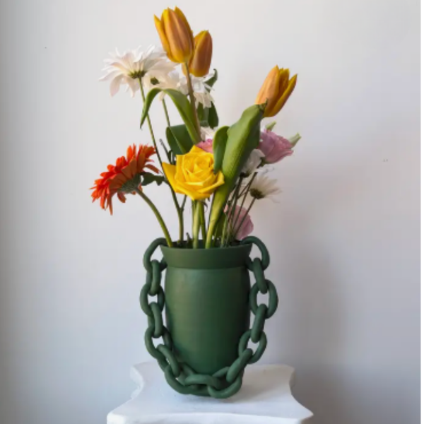 The Terroso Studios Green Vase, featuring handmade chain-like handles, displays yellow tulips, a yellow rose, a red gerbera daisy, plus white and pink blooms in front of a plain background.