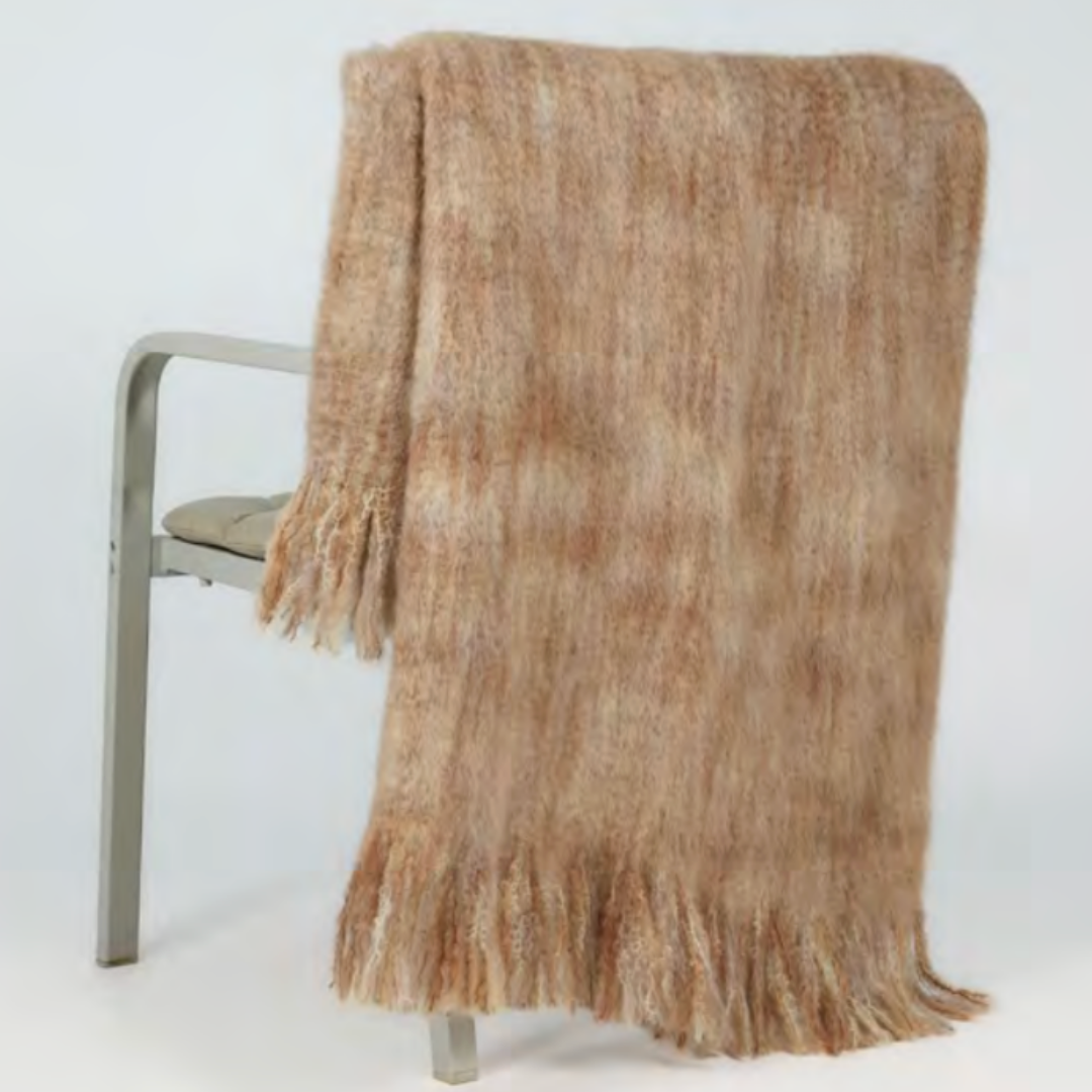The Mantas Ezcaray 5th Elements Throw, a soft brown and beige wool blanket with artisanal craftsmanship, is draped over the back of a light-colored chair.