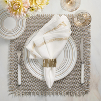 Elegant table setting featuring a white and gold-rimmed plate, folded white napkin adorned with the Matrix Napkin Ring in Gold by Kim Seybert, silverware, wine glass, fresh flowers, and a textured placemat.