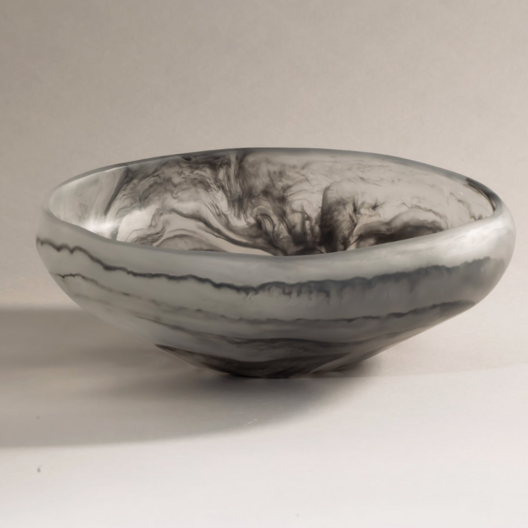 The Mayan Resin Bowl by CDMX / MONICA CALDERON is a round, shallow handmade piece from Mexico, featuring smooth surfaces with swirling black and gray marbled patterns on a light backdrop.