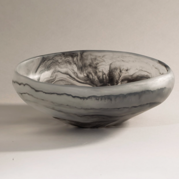 The Mayan Resin Bowl by CDMX / MONICA CALDERON is a round, shallow handmade piece from Mexico, featuring smooth surfaces with swirling black and gray marbled patterns on a light backdrop.