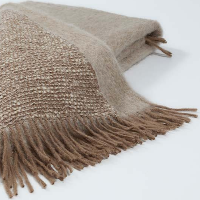A close-up of the Coco Throw by Mantas Ezcaray, a tan and beige double-sided blanket with fringe, crafted from soft Chanel fabric for a luxurious feel.