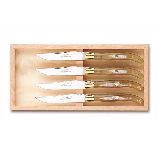 The Claude Dozorme Laguiole Specialty Steak Knives Brass Bolster Set/4 Light Horn comes in a wooden box, with four knives featuring shiny metal blades and curved handles, each neatly arranged in its own slot.