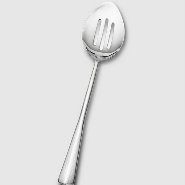 The Mary Jurek Alta Slotted Serving Spoon features a textured handle and sleek stainless steel design, shown against a plain light gray background—a stylish addition to your serveware collection.