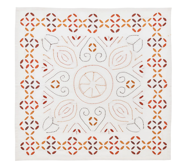 The Kim Seybert Malta Embroidered Napkin Set of 4 features white handcrafted napkins with orange, brown, and black symmetrical floral and geometric embroidery in a central circular motif.