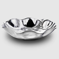 The Mary Jurek Blossom Stainless Steel Bowl features wavy edges and a hammered, reflective surface. Shiny and eye-catching, it is both dishwasher safe and elegantly displayed against a plain light gray background.