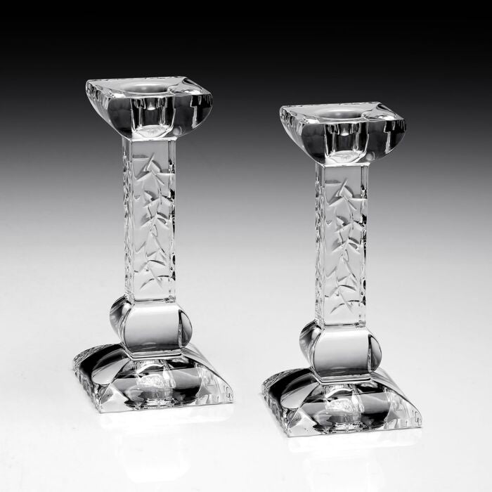 The Nicola Candlesticks Set of 2 by William Yeoward features clear glass with square bases and textured stems, standing upright on a reflective surface—an elegant touch to your décor or a thoughtful wedding gift, set against a black-to-white gradient background.