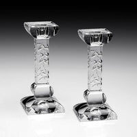 The Nicola Candlesticks Set of 2 by William Yeoward features clear glass with square bases and textured stems, standing upright on a reflective surface—an elegant touch to your décor or a thoughtful wedding gift, set against a black-to-white gradient background.