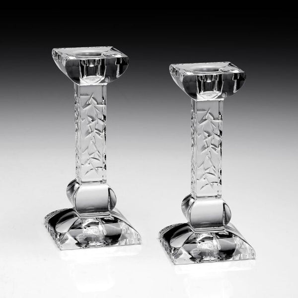 The Nicola Candlesticks Set of 2 by William Yeoward features clear glass with square bases and textured stems, standing upright on a reflective surface—an elegant touch to your décor or a thoughtful wedding gift, set against a black-to-white gradient background.