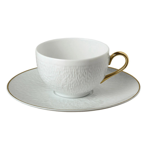 A white textured porcelain teacup with a gold handle sits on a matching Raynaud Mineral Irise Gold Filet saucer, featuring a delicate gold rim—a sophisticated addition to any modern dinnerware collection.