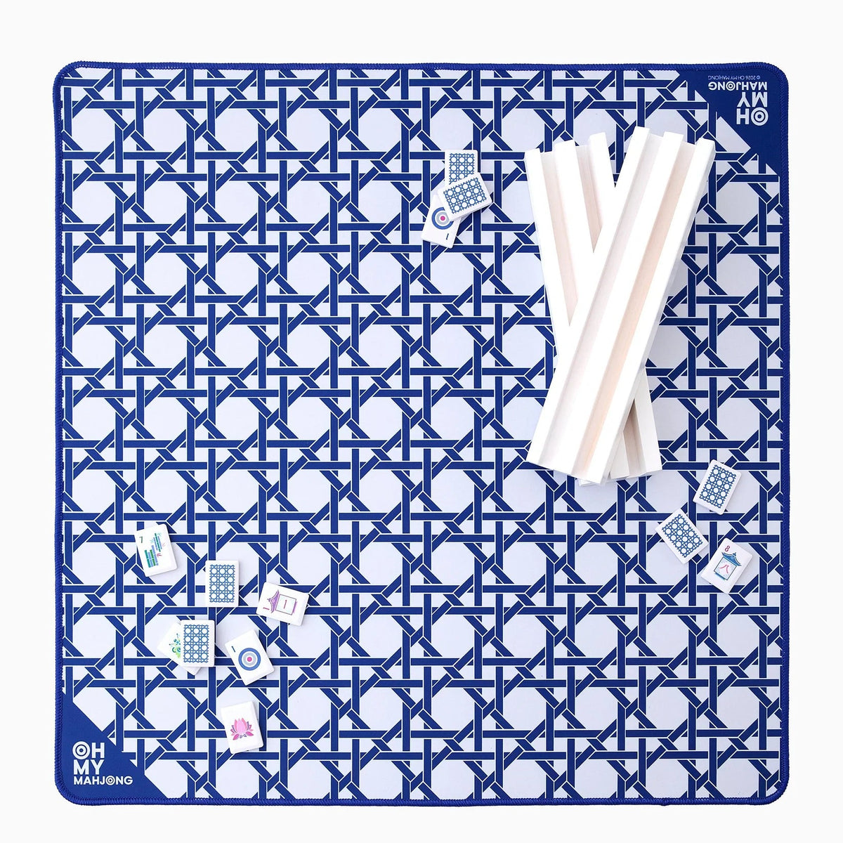 The Oh My Mahjong Travel Mini Mahjong Game Mat, sized 22” x 22”, features a blue and white pattern with logo, Mahjong tiles, and white racks displayed on the portable mat.