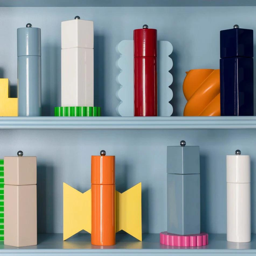 Addison Ross Mini Pillar Salt & Pepper Shakers, featuring a white lacquer finish and ceramic grinder, are displayed on blue shelves for a playful, modern look with bold colors and geometric design.