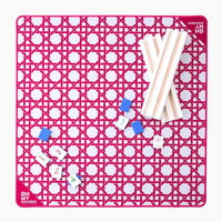 The Oh My Mahjong Travel Mini Mahjong Game Mat (22” x 22”) features a pink geometric pattern, white racks on the right, blue tile holders and tiles on the left, and “Oh My Mahjong” printed in the bottom left—ideal for portable play.