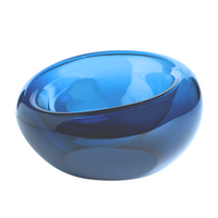 The Axiom Glass Caldera Vessel Medium 9" features a deep blue, hand-blown glass design with a smooth, organic shape. Its clear, translucent bowl lets light shine through, making it a striking piece of artisan glass decor.