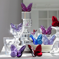 Papilion Lucky Butterfly crystal figurines by Baccarat in purple, red, and blue are beautifully displayed on clear glassware and stacked plates, creating an elegant lucky-charm gift on a reflective white surface.