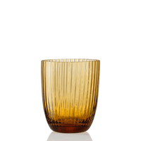 Idra Tumbler Rigadin by Nason Moretti, an amber-colored glass tumbler featuring a modern, transparent design with vertical ribbed detailing, a smooth rim, and a slightly rounded base, shown standing upright on a white background.